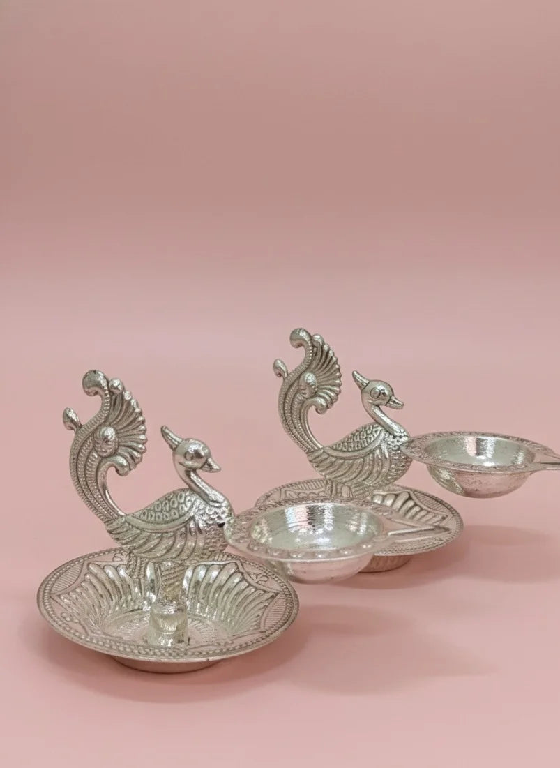 Silver peacock-shaped candle holders on a pink background