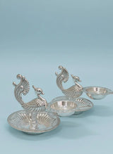 Set of three silver peacock-shaped bowls on a light blue background