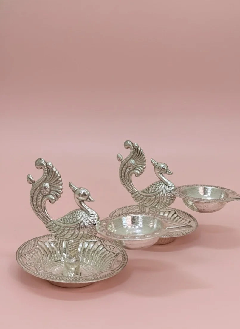 Silver peacock-shaped candle holders on a pink background