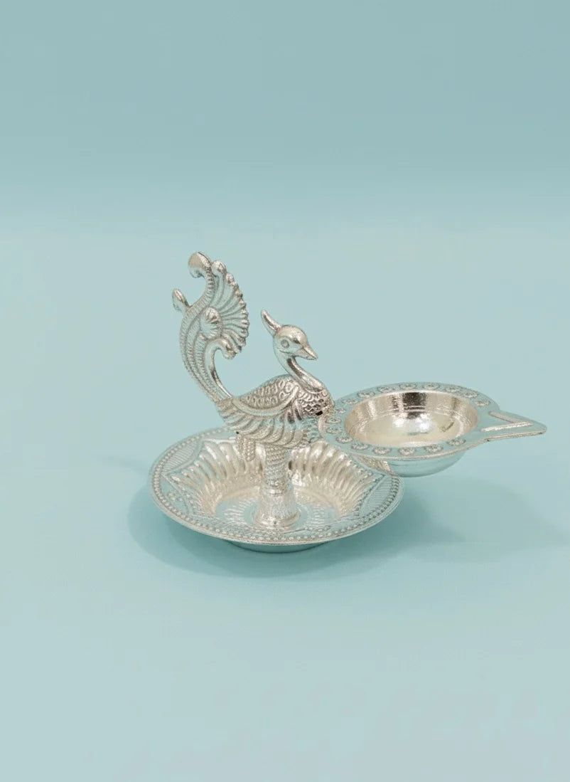 Decorative silver peacock-shaped oil lamp on a light blue background