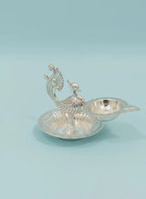 Decorative silver peacock-shaped oil lamp on a light blue background