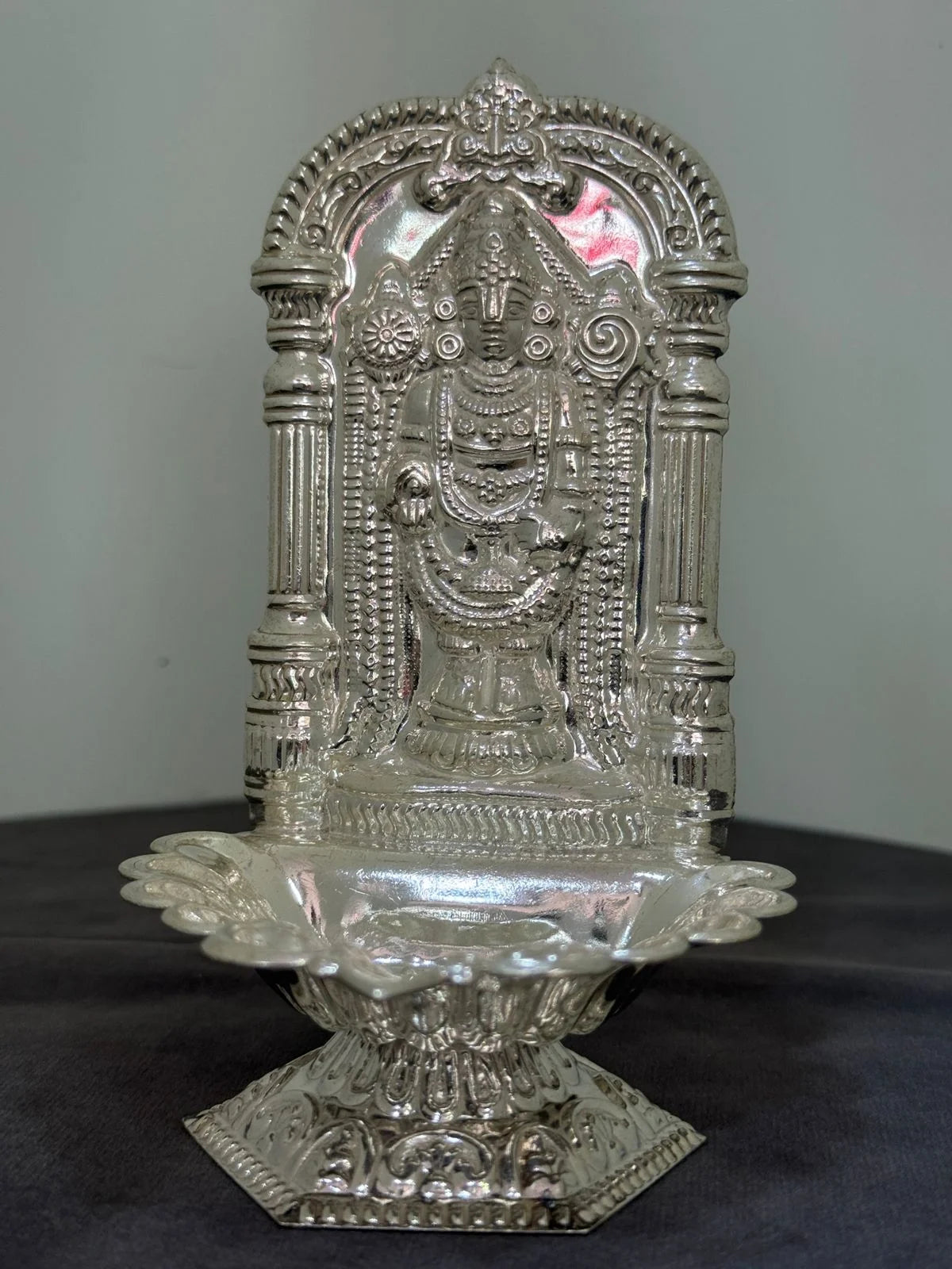 Decorative silver神像 on a dark surface with a plain background