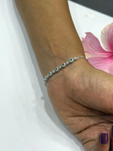 Hand wearing a silver bracelet with green stones on a white surface with pink petals.