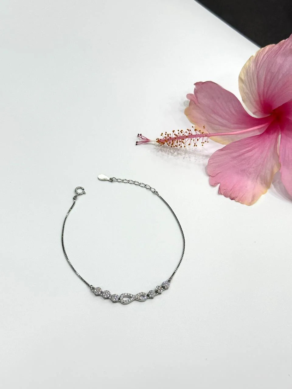 Silver bracelet on a white surface with a pink flower
