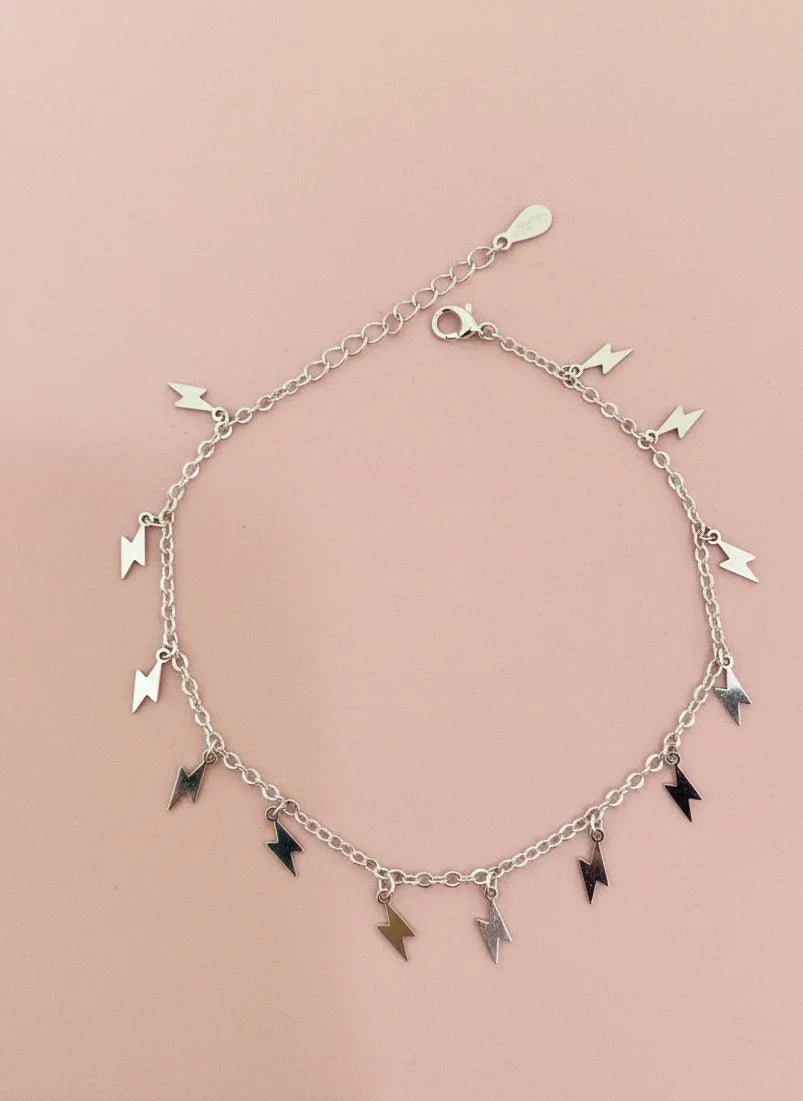 Silver bracelet with lightning-shaped charms on a pink background