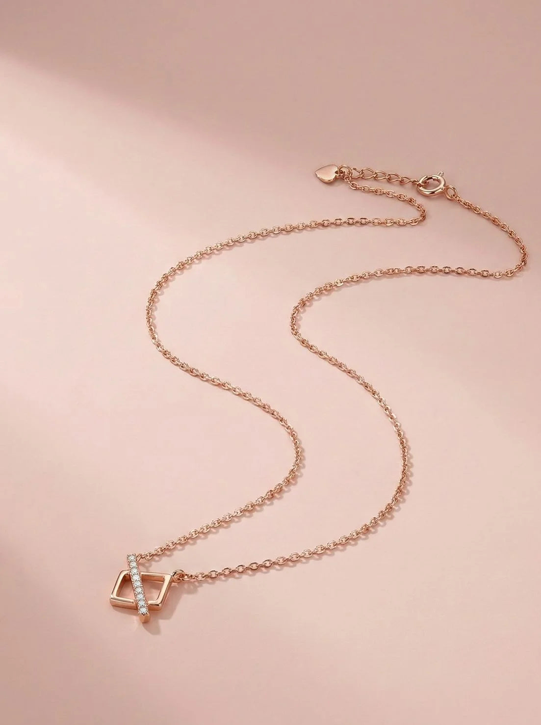 Rose gold necklace with a pendant on a pink background