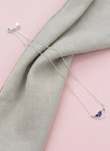 Silver necklace with a purple gemstone on a light gray fabric background