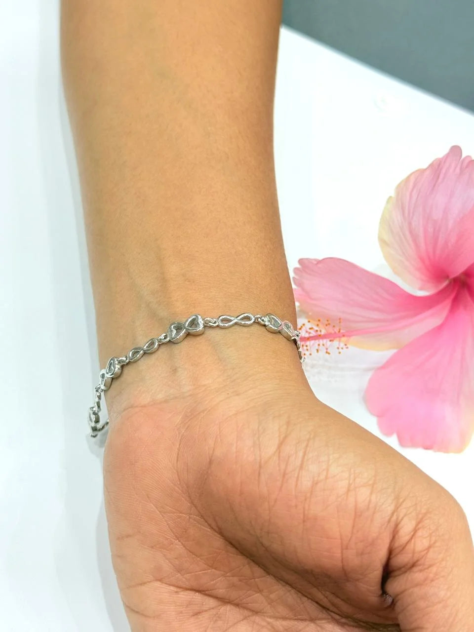 Silver bracelet on a wrist with a pink flower in the background
