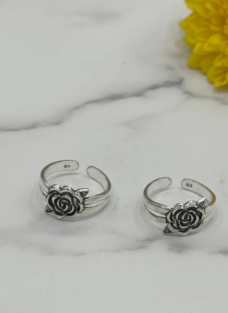 Silver rose-shaped toe rings on a marble surface with a yellow flower.