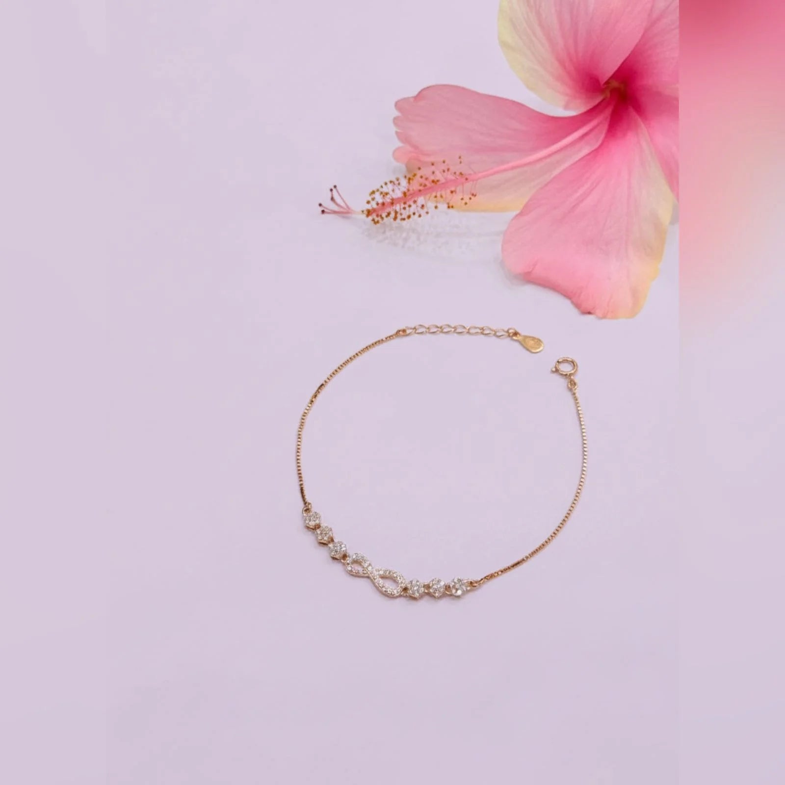 Gold bracelet with small stones on a light pink background with a pink flower.