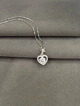 Heart-shaped diamond pendant on a chain against a gray background