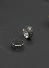 Two silver toe rings with intricate designs on a dark textured surface with a yellow flower.