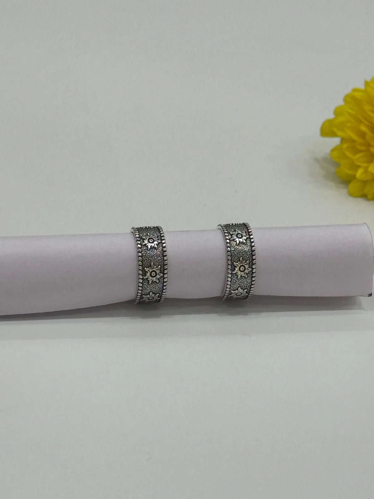 Decorative silver toe rings on a white cylindrical object with a yellow flower in the background