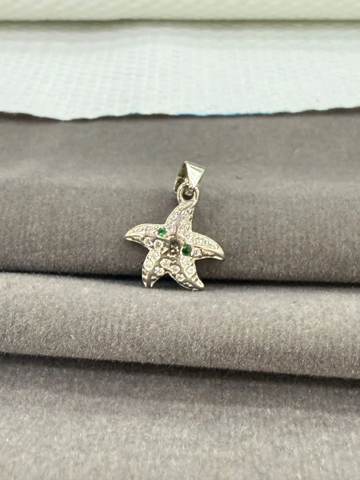 Starfish-shaped pendant with green stones on a textured surface