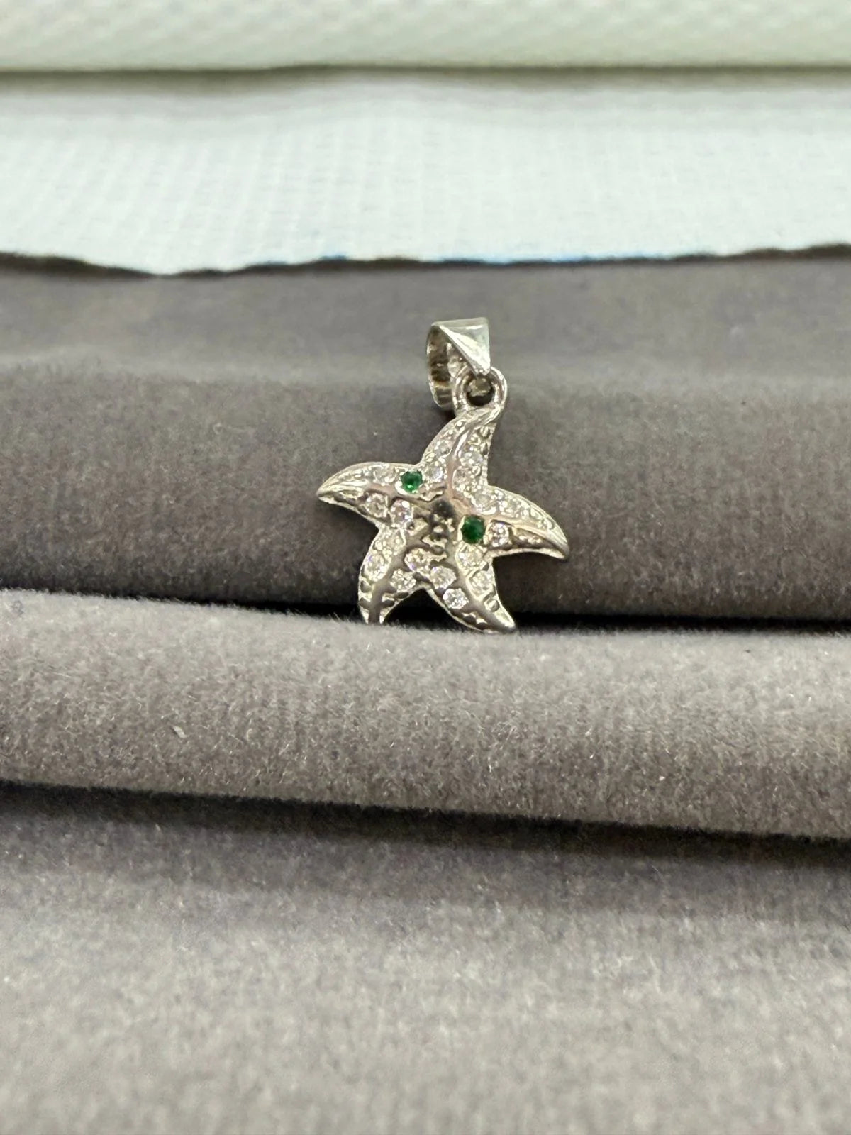 Starfish-shaped pendant with green stones on a gray surface