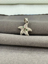 Starfish-shaped pendant with green stones on a gray surface