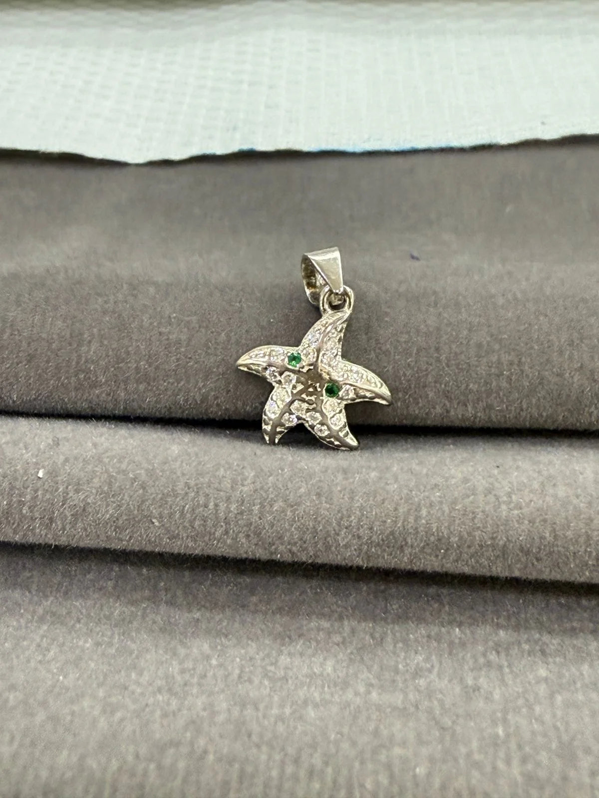 Starfish-shaped pendant with green stones on a textured surface