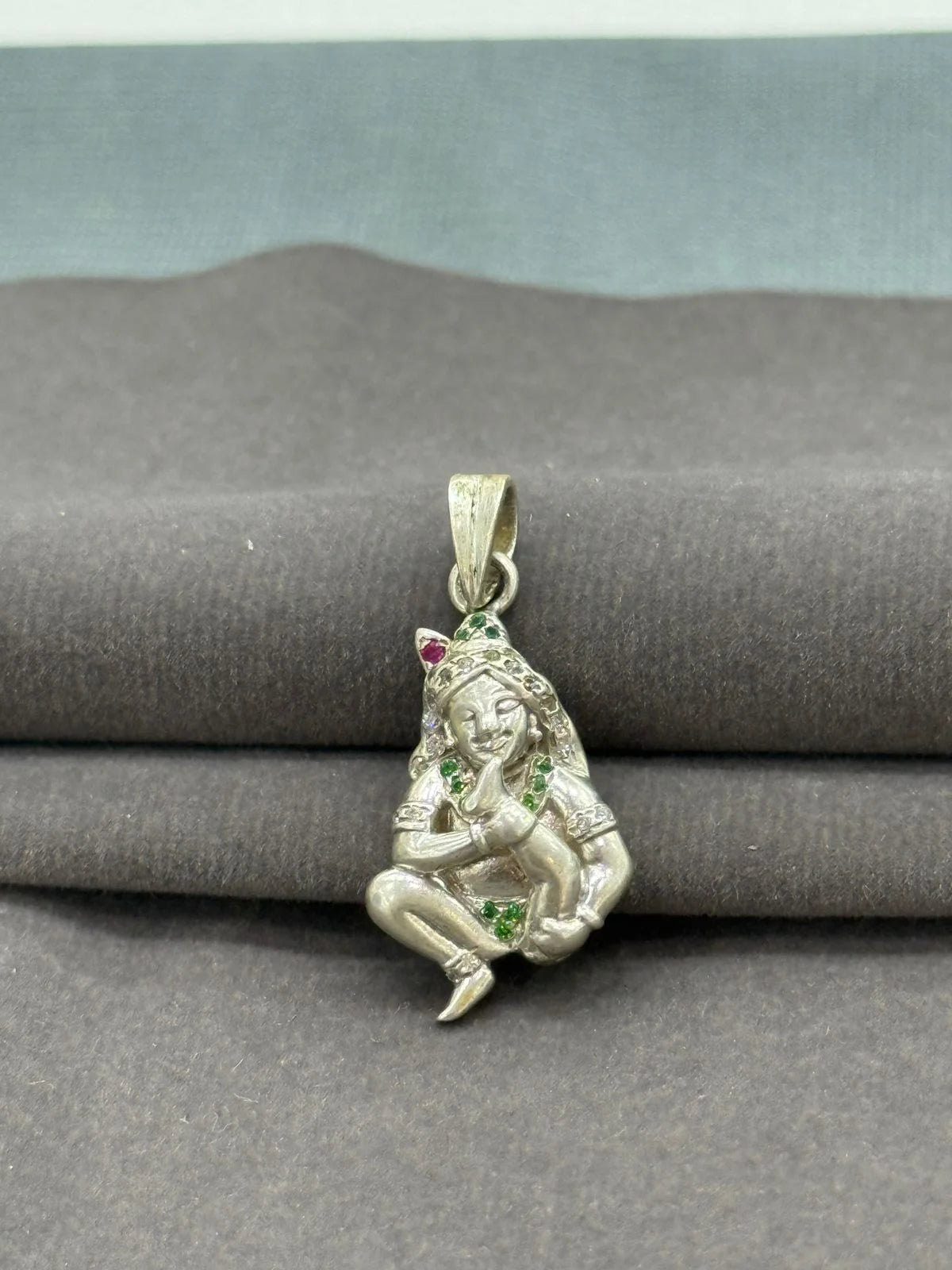 Silver pendant with a figure holding a fruit on a gray surface