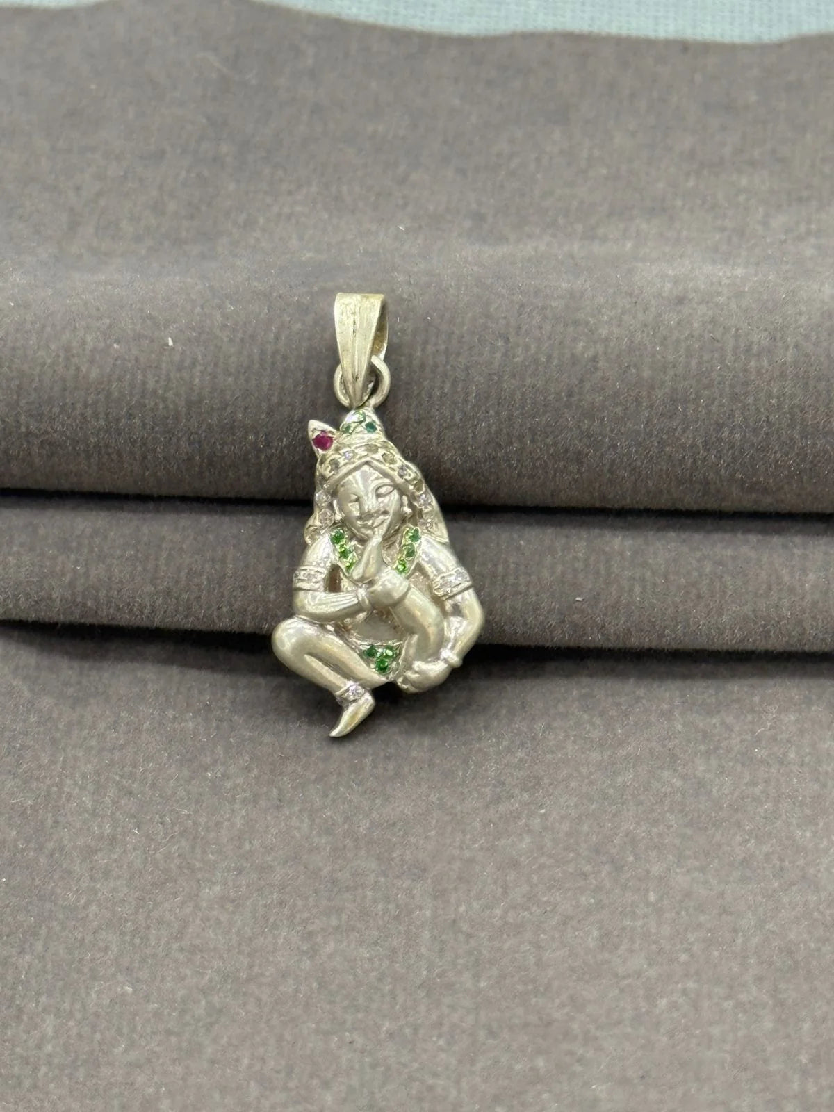 Silver pendant with green and red stones on a gray fabric background