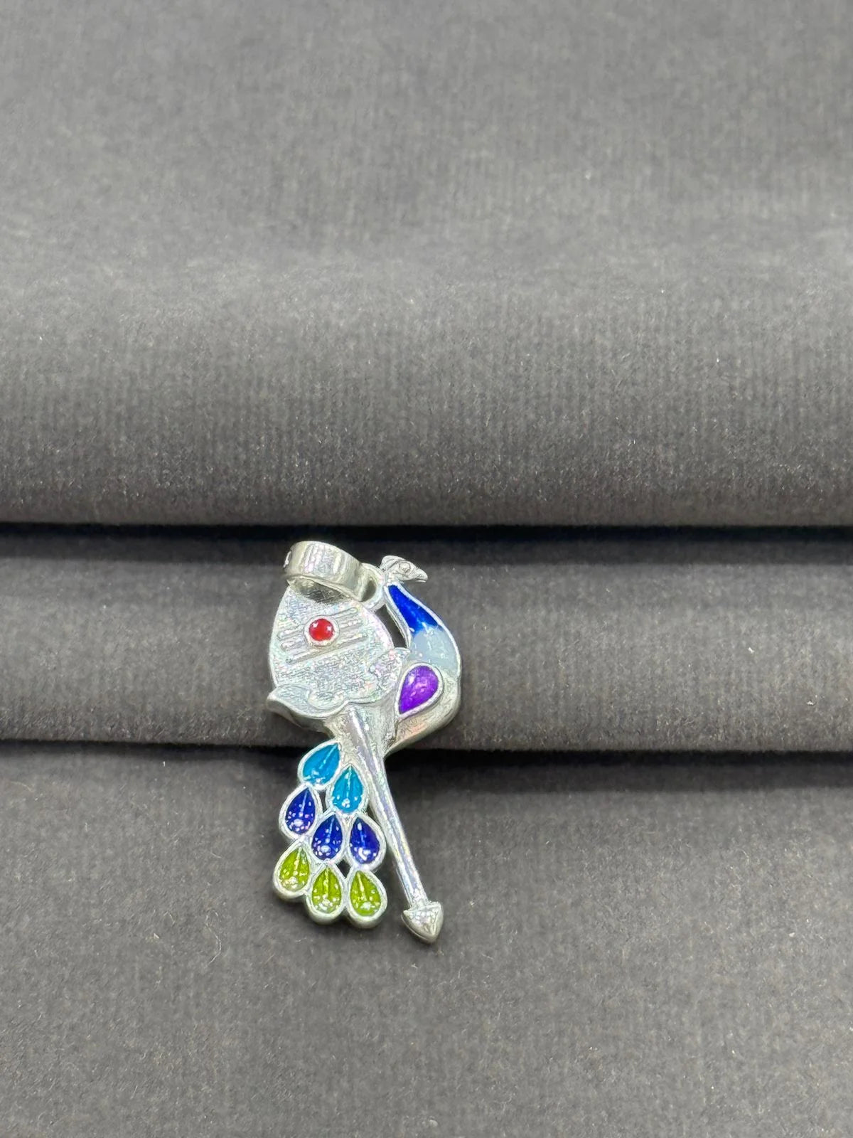 Colorful pendant with a peacock feather design on a gray fabric background