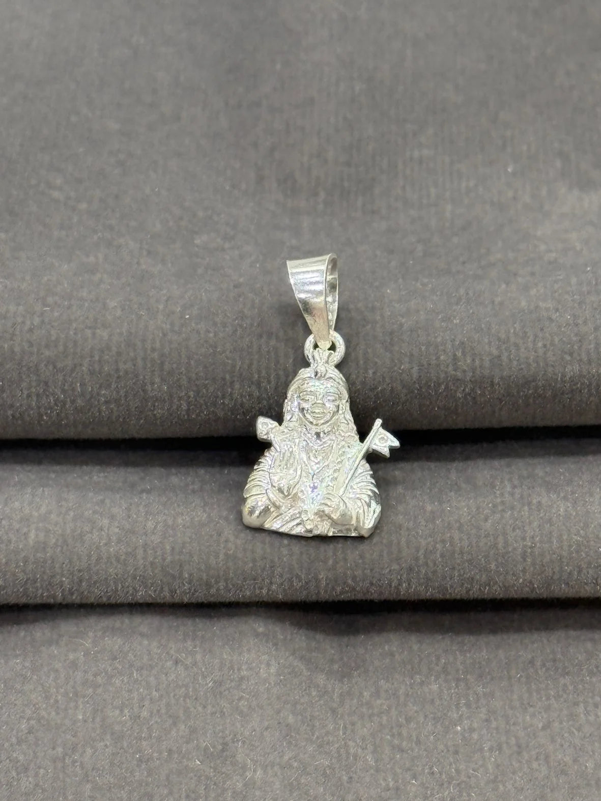 Silver pendant of a seated figure on a gray fabric background