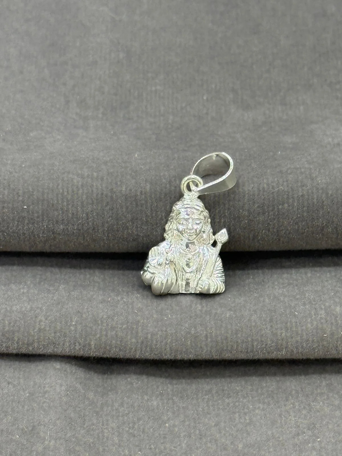 Silver pendant of a deity on a gray fabric background