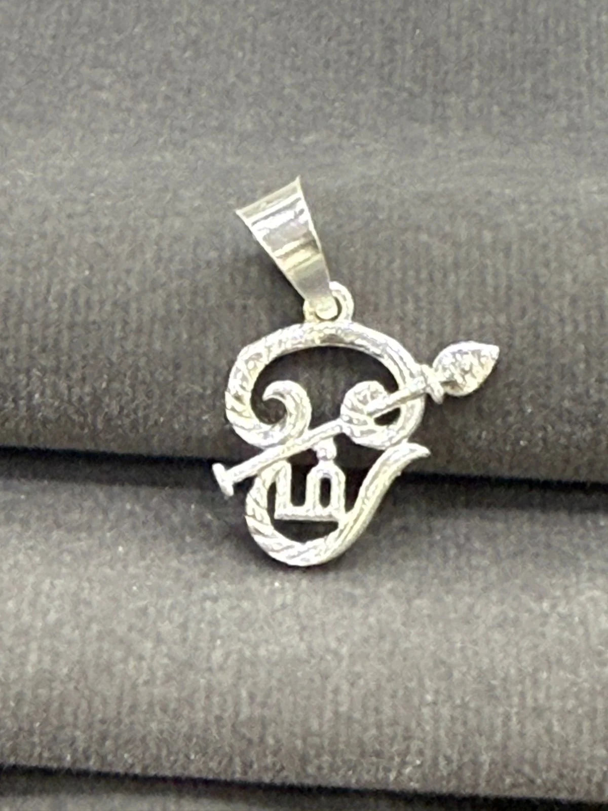Silver pendant with leaf design on a gray fabric background