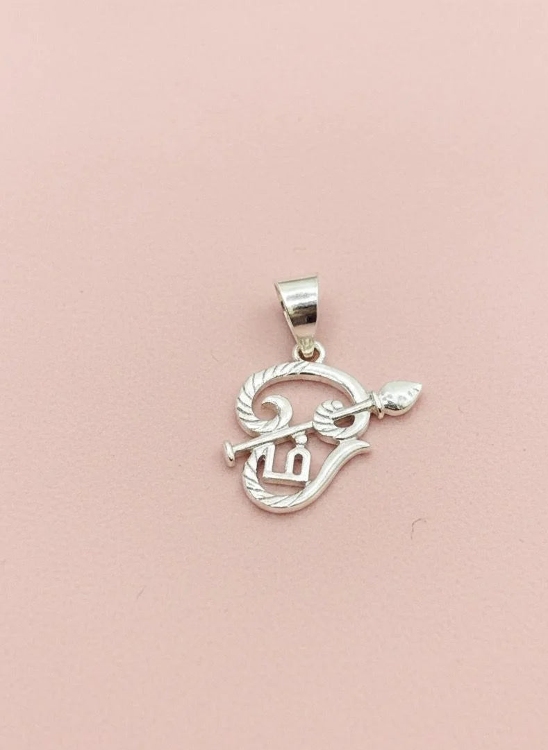 Silver pendant with intricate design on a pink background