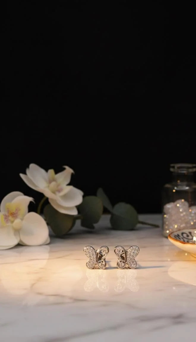 Butterfly-shaped earrings on a marble surface with flowers and a candle in the background