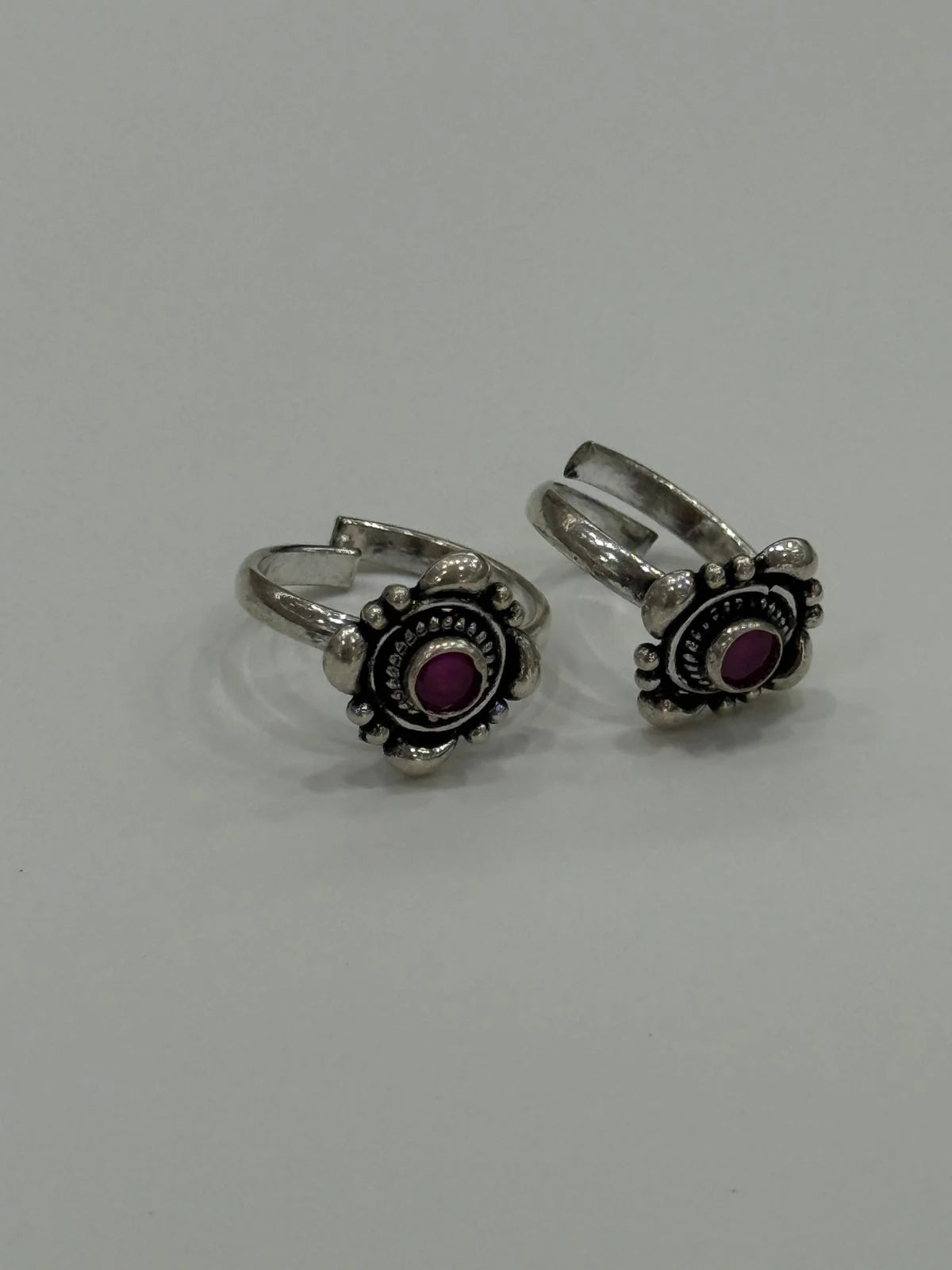 Pair of silver toe rings with purple stones on a light gray background