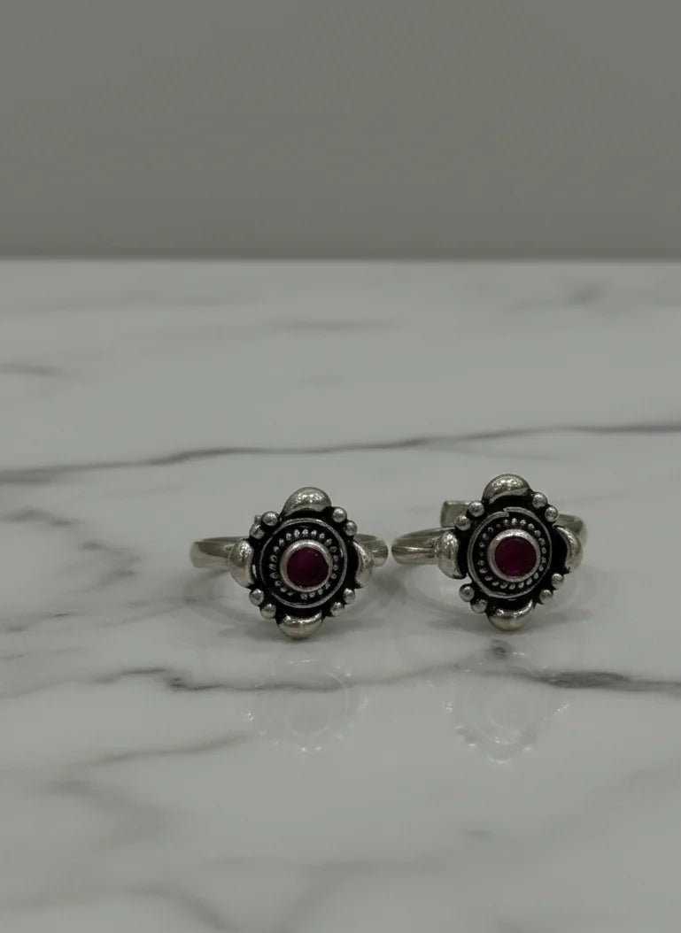 Pair of silver toe rings with red gemstones on a marble surface