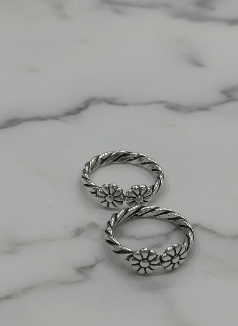 Silver toe ring with floral designs on a marble surface