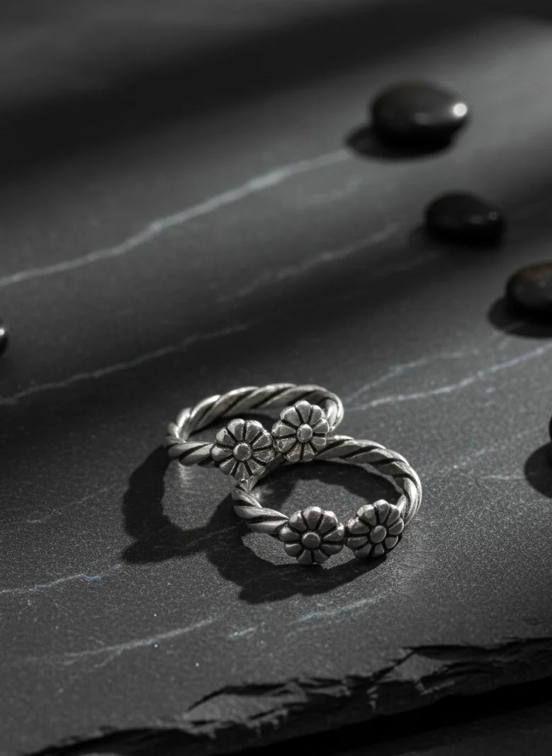 Silver toe ring with floral designs on a dark stone surface