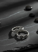 Silver toe ring with floral designs on a dark stone surface
