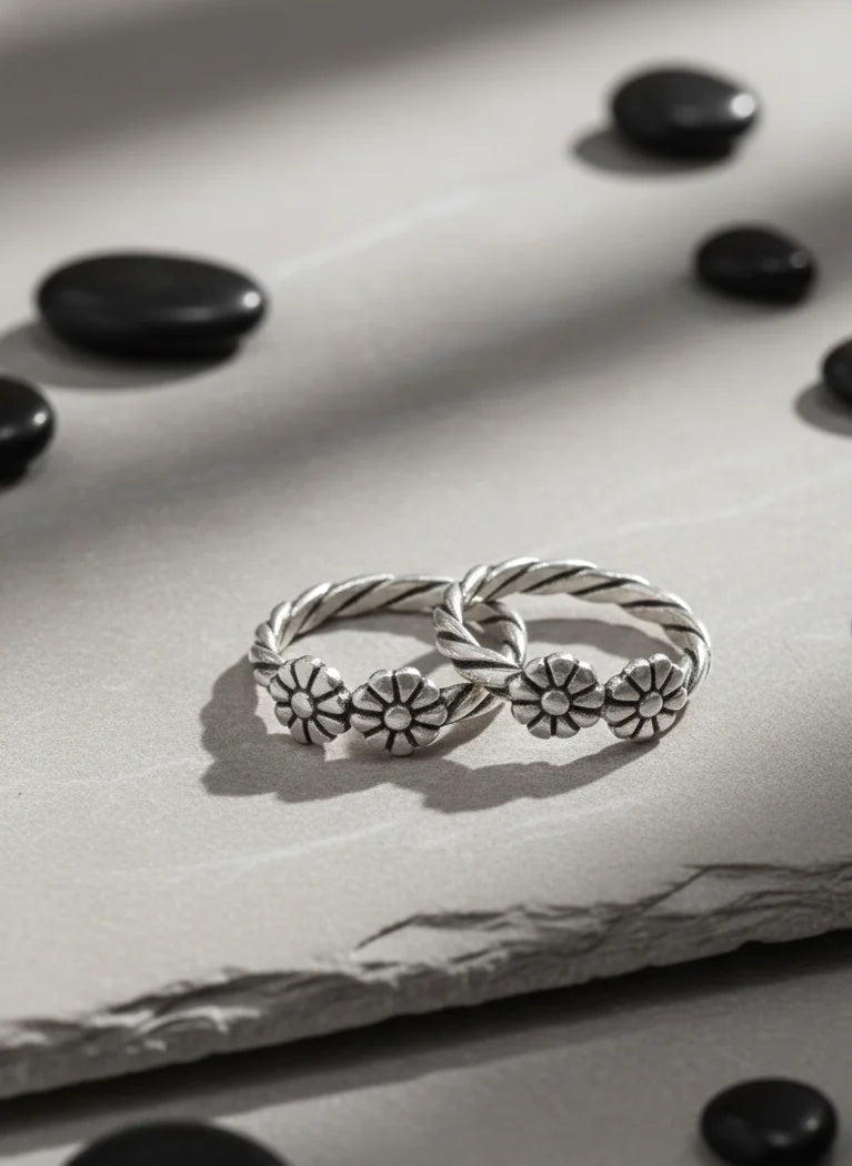 Silver toe ring with floral designs on a textured surface with black stones.