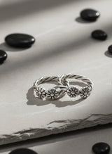 Silver toe ring with floral designs on a textured surface with black stones.