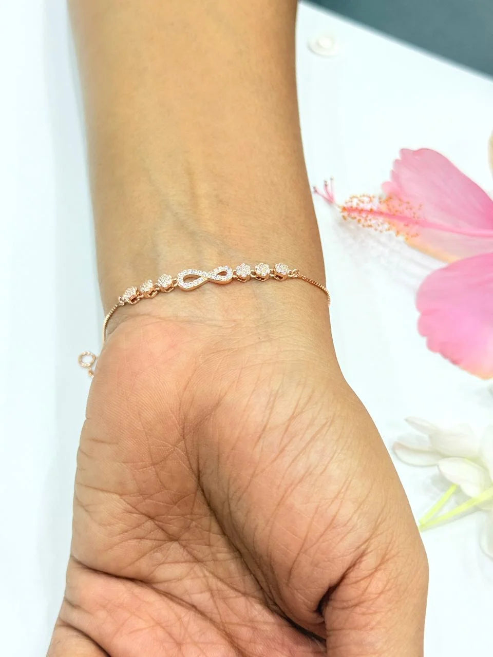 Hand wearing a delicate bracelet with a blurred pink flower in the background