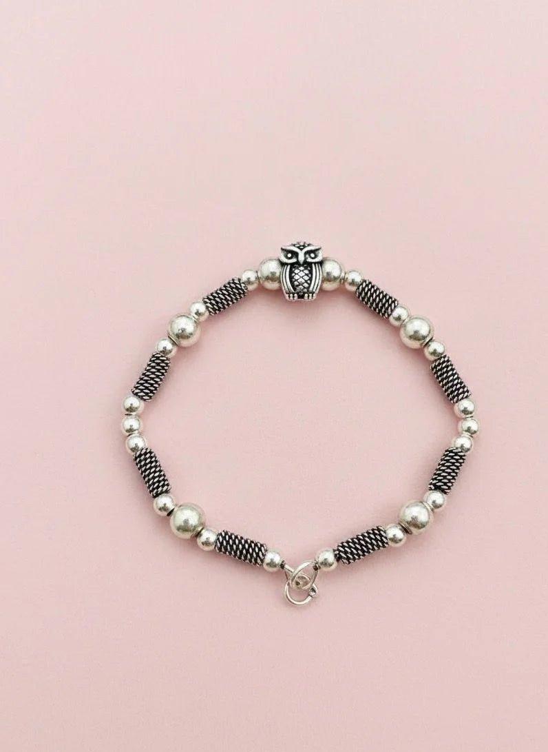 Beaded bracelet with an owl charm on a pink background