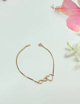 Gold bracelet with a heart and infinity symbol on a light background with flowers.